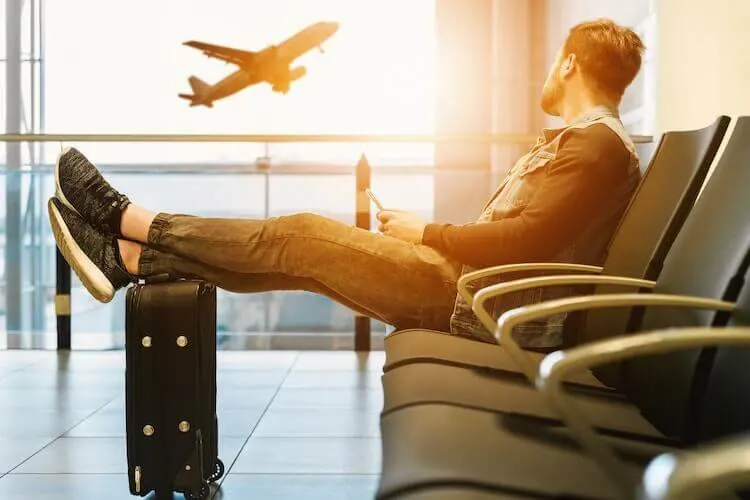 Man watching plane while sitting in airport with legs propped up on suitcase