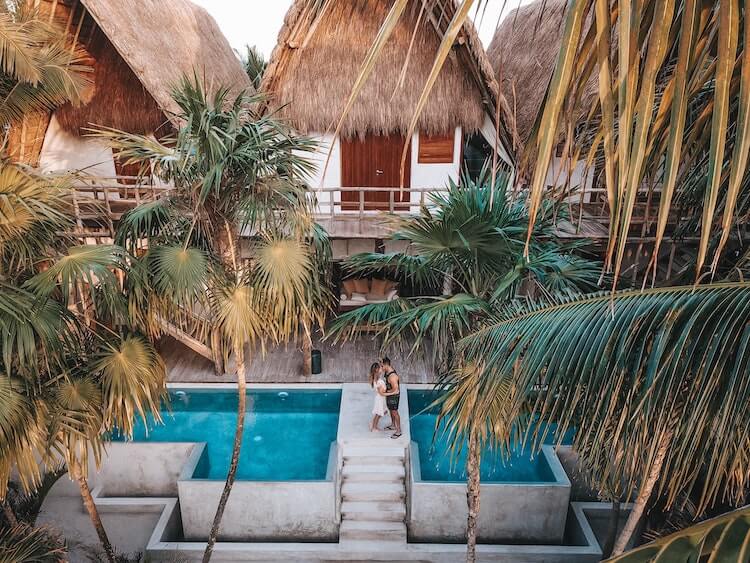 Couple kissing over a pool bridge with bungalows in the background and palm trees