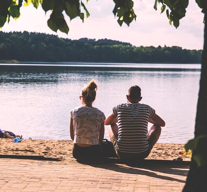 man and woman sitting at edge of lake