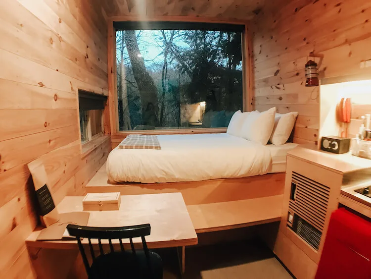 A look inside of Getaway House Ohio with table and seating, queen bed, big window, and kitchen