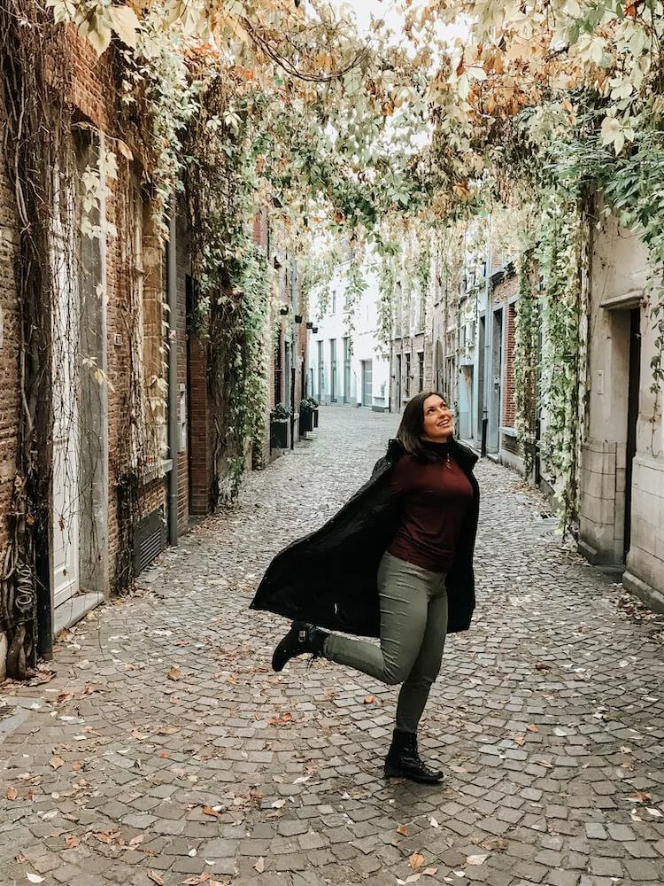 Kat twirling around under a canopy of plants on a cobblestone street in Antwerp- Antwerp in one day