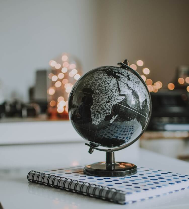 Globe on top of book with lights in the background- ways to bring travel to you at home