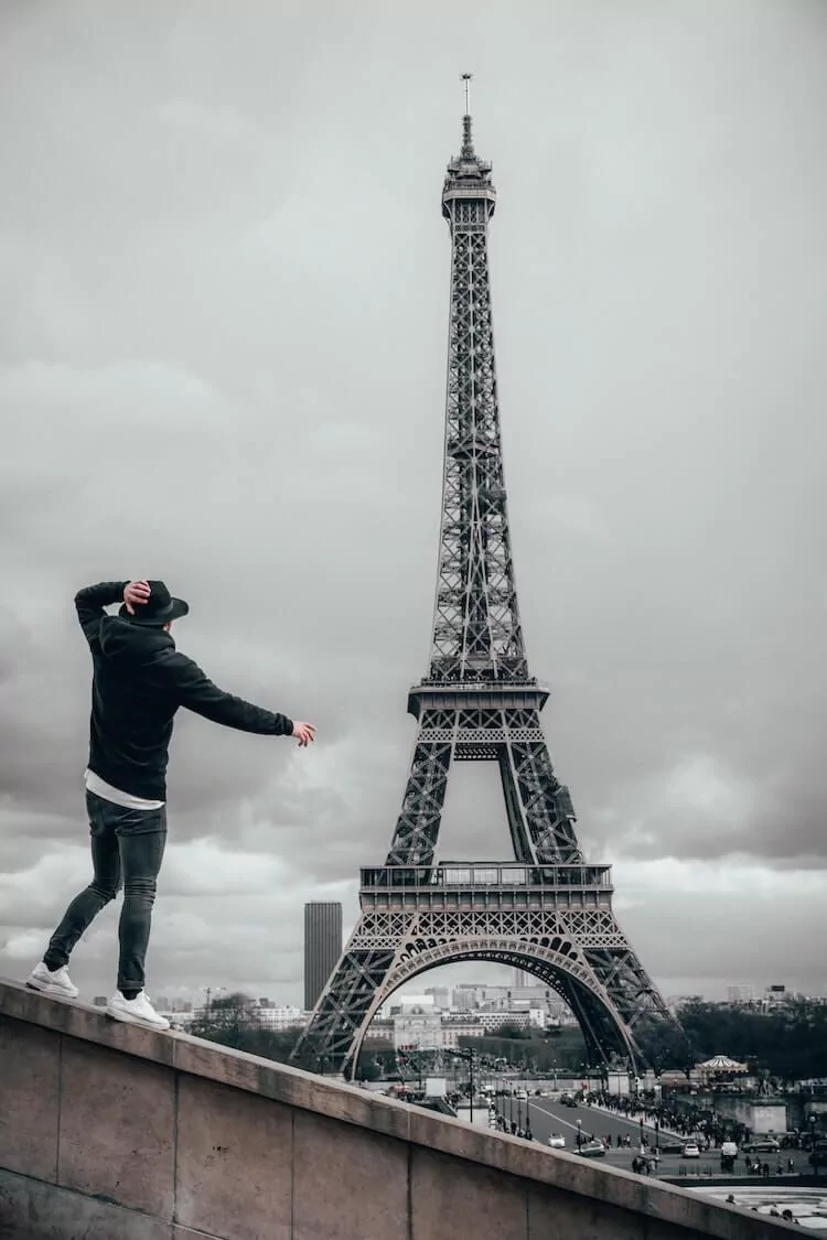 Man wearing jeans, sweater, and hat in front of the Eiffel Tower
