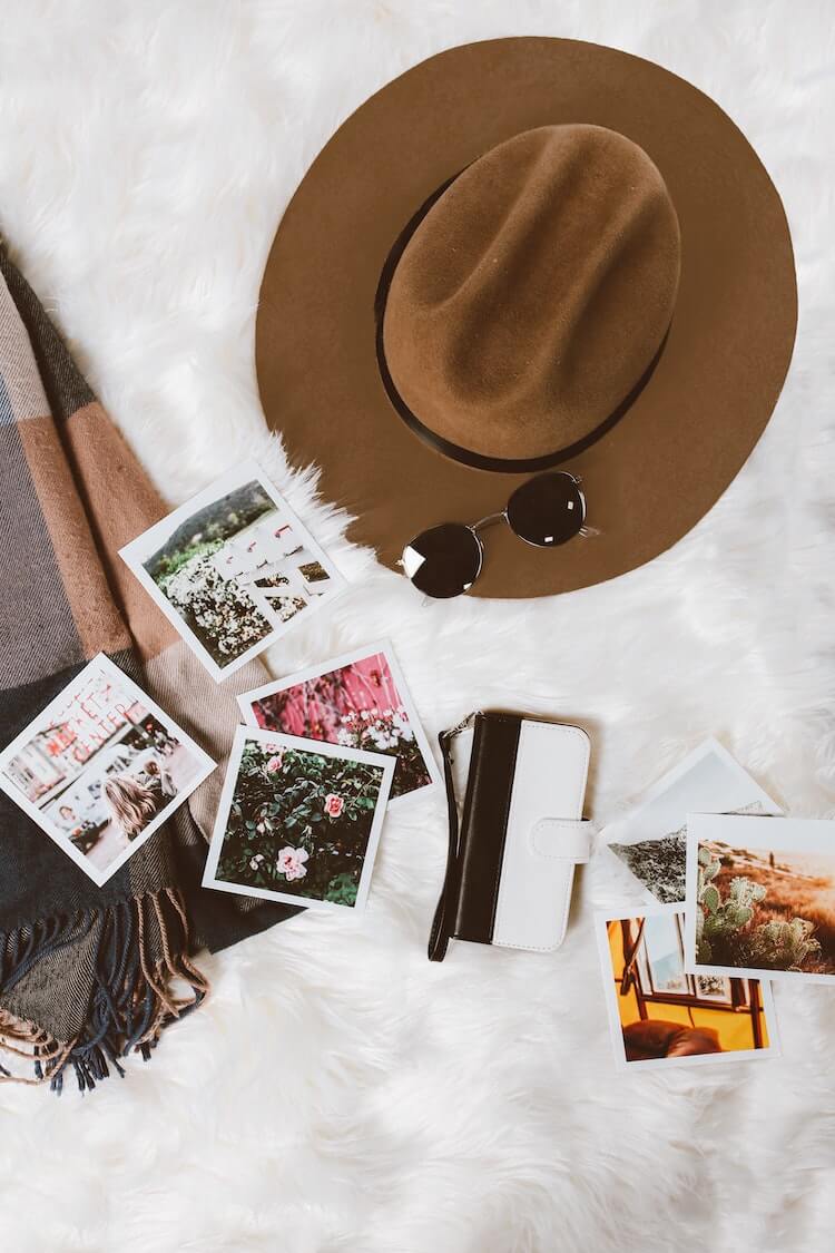 What Travel Bloggers are Thankful For - Brown Hat and Sunglasses with Travel Photos on a White Blanket