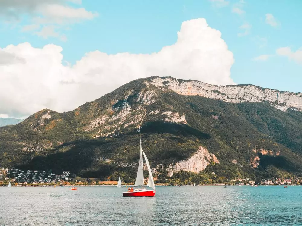 Lake Annecy with a sailboat on the water and a mountain in the background