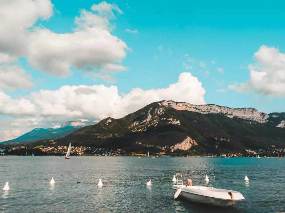 Mountains and a mountain lake with a small boat in the foreground | Things to do in Annecy