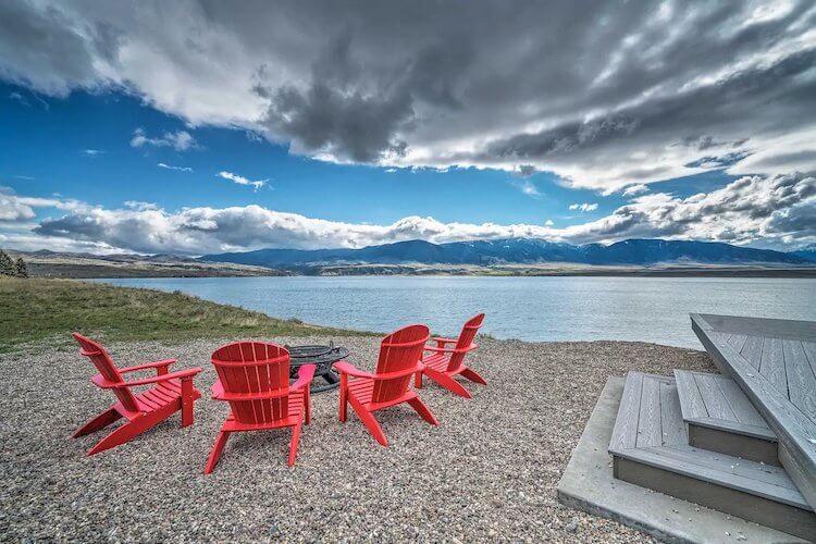 Red deck chairs arranged around a fire pit facing the lake and mountains in Montana