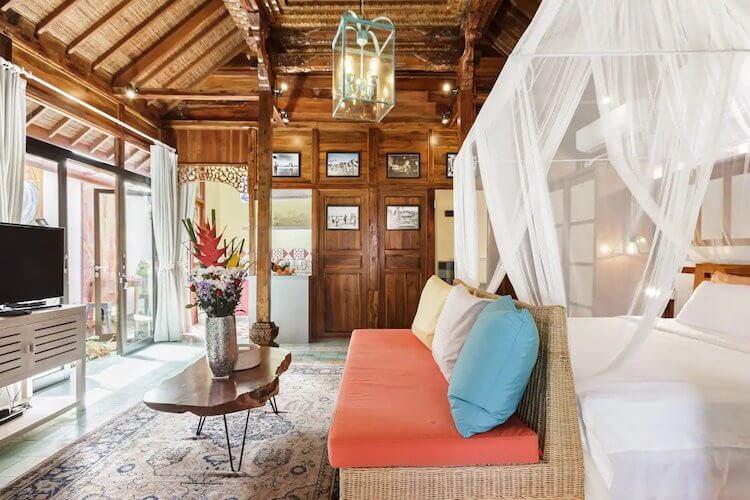 Teak walls and ceiling in a large room with a white bed with bug net in a Bali Airbnb