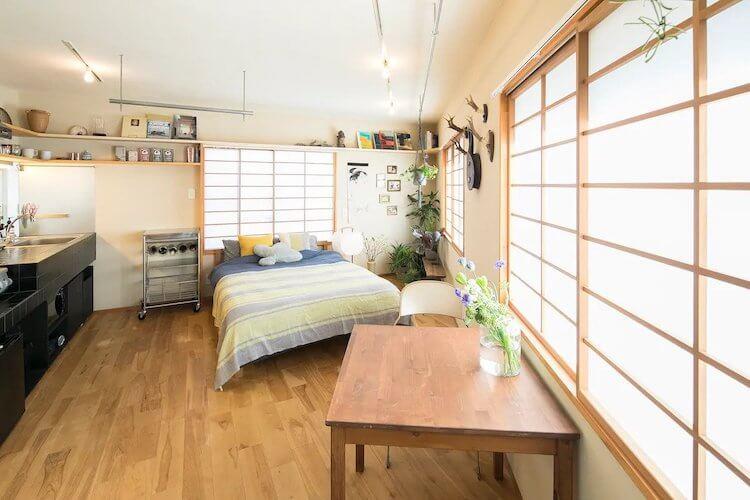 Tokyo Airbnb featuring bright panels on the walls with light, a kitchenette, a green and blue bed, and a table with flowers