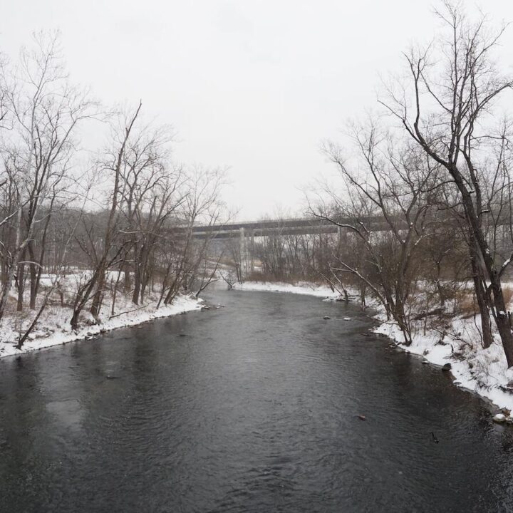 Things to do in Cuyahoga Valley National Park in Winter | creek flowing with snowy landscape on either side and bridge in the background