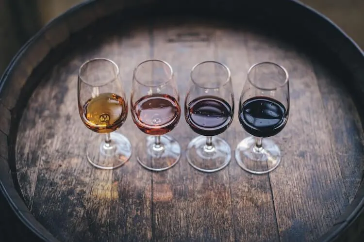 4 wine glasses filled with varying types of wine sitting on a barrel