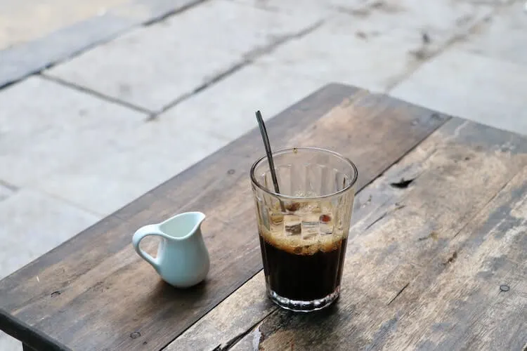 Vietnamese iced coffee sitting on a table next to a milk pourer