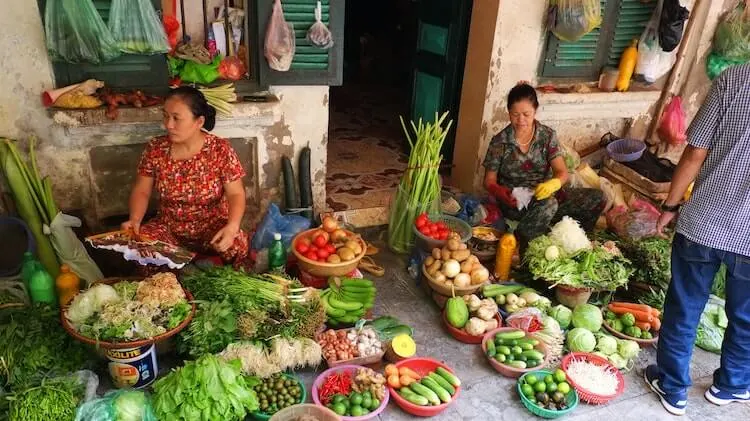 Women sitting down around fruits and vegetables at a market in Hanoi