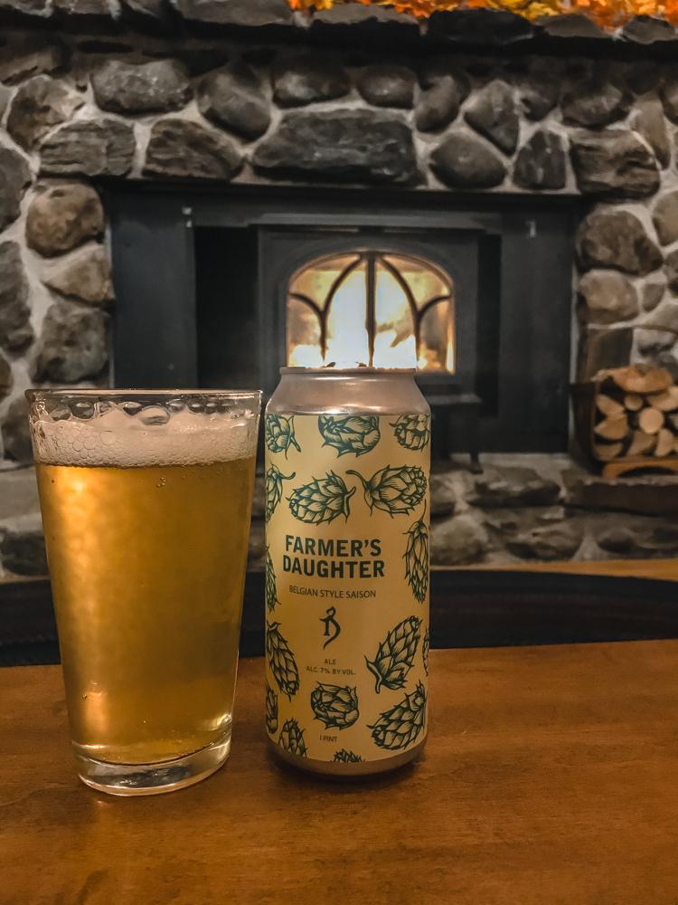 Farmer's Daughter beer can with full beer glass in front of a stone fireplace