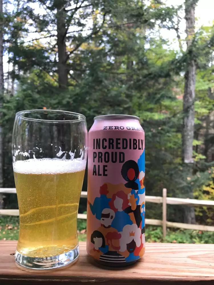 Incredibly Proud Ale can next to a three quarter's full beer glass in front of the woods