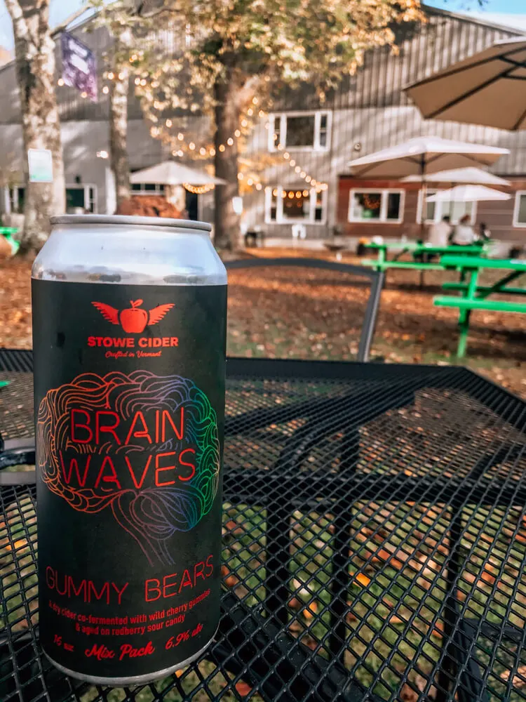 Stowe Cider Brain Waves Can in the back of the cidery with lights in the background. can is sitting on a black patio table - Things to do in Stowe VT - Weekend in Stowe