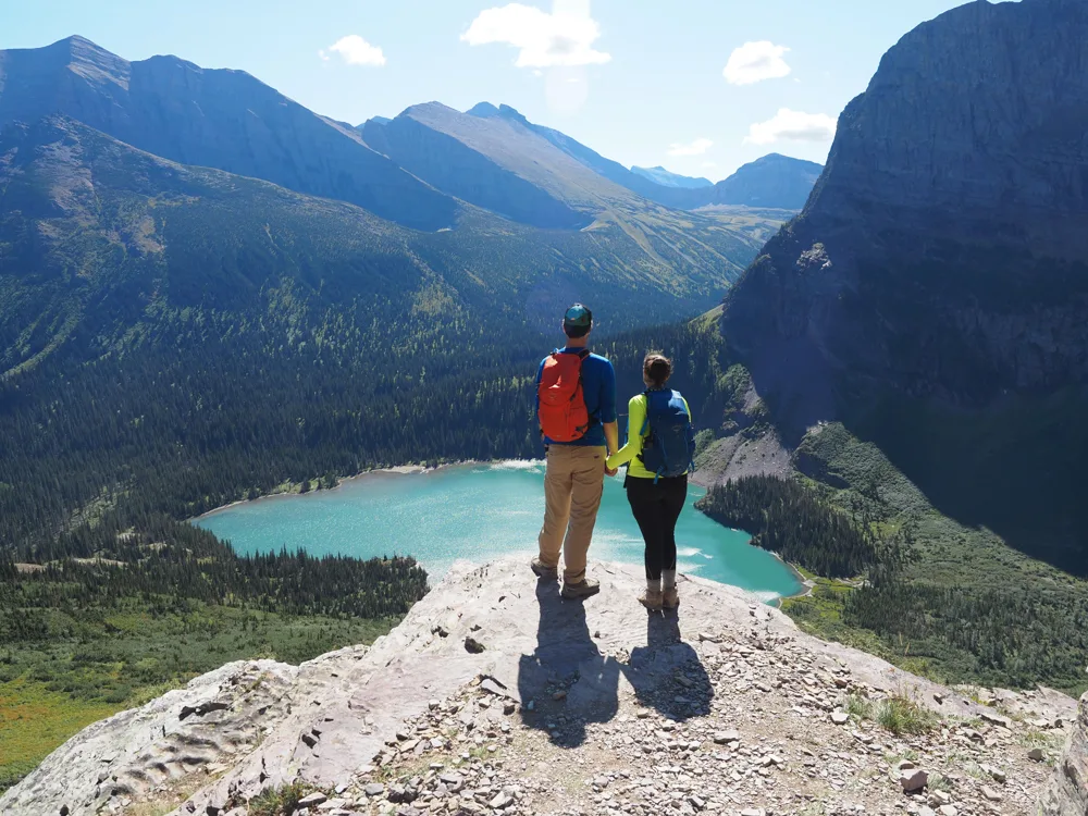 Kat and Chris holding hands and looking at a lake on the Grinnell Glacier Trail