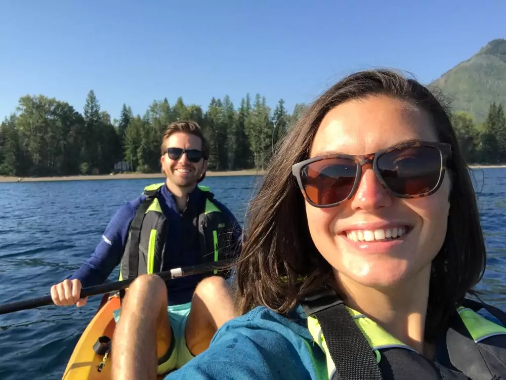 Kat and Chris smiling at the camera and wearing sunglasses while kayaking on Lake McDonald
