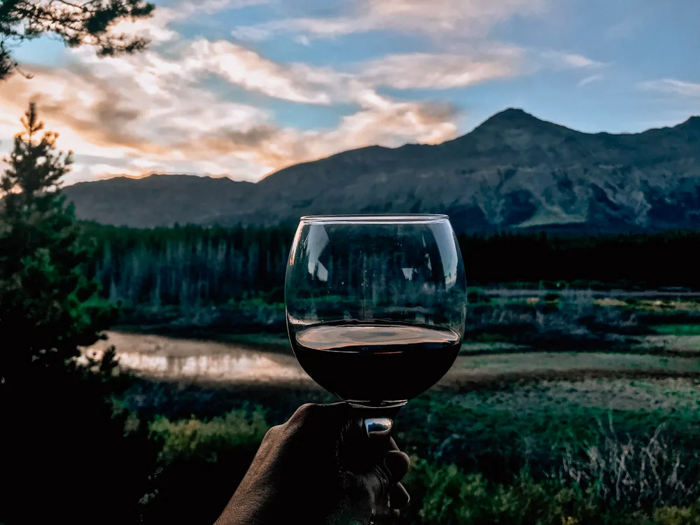 Red wine in a glass being held in a hand with the sunset over the mountains at Summit Mountain Lodge and Steakhouse