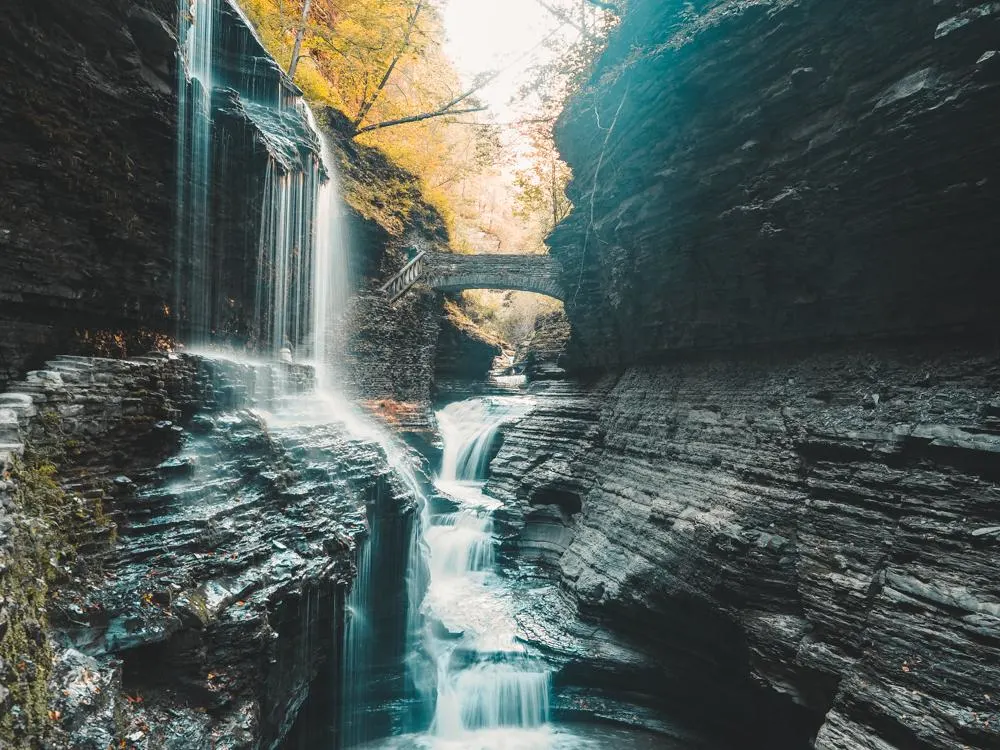 Rainbow Falls with a waterfall over the trail and the bridge in the distance