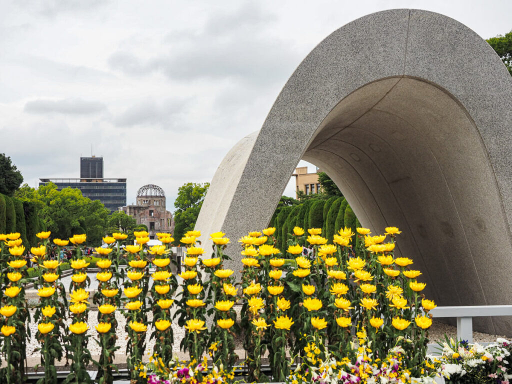 Hiroshima Peace Memorial Park with arch and yellow flowers with the A-Bomb dome in the distance